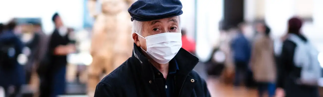 An old man standing in a museum wearing face mask
