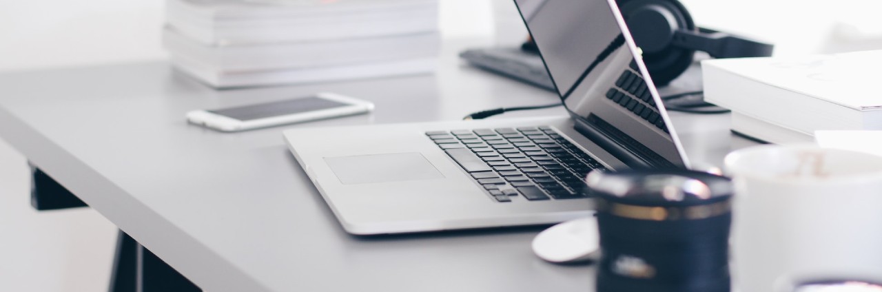 A laptop, phone, coffee mug and headphones kept on a white table