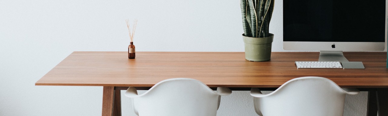 A desk with a computer set up, a plant and a diffuser