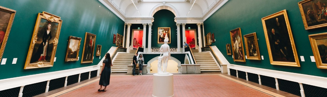 A museum with paintings and sculptures and a woman looking at one of the paintings A museum with paintings and sculptures and a woman looking at one of the paintings