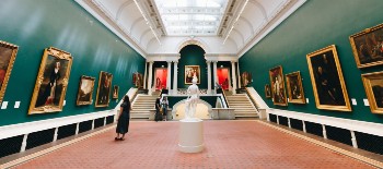 A museum with paintings and sculptures and a woman looking at one of the paintings